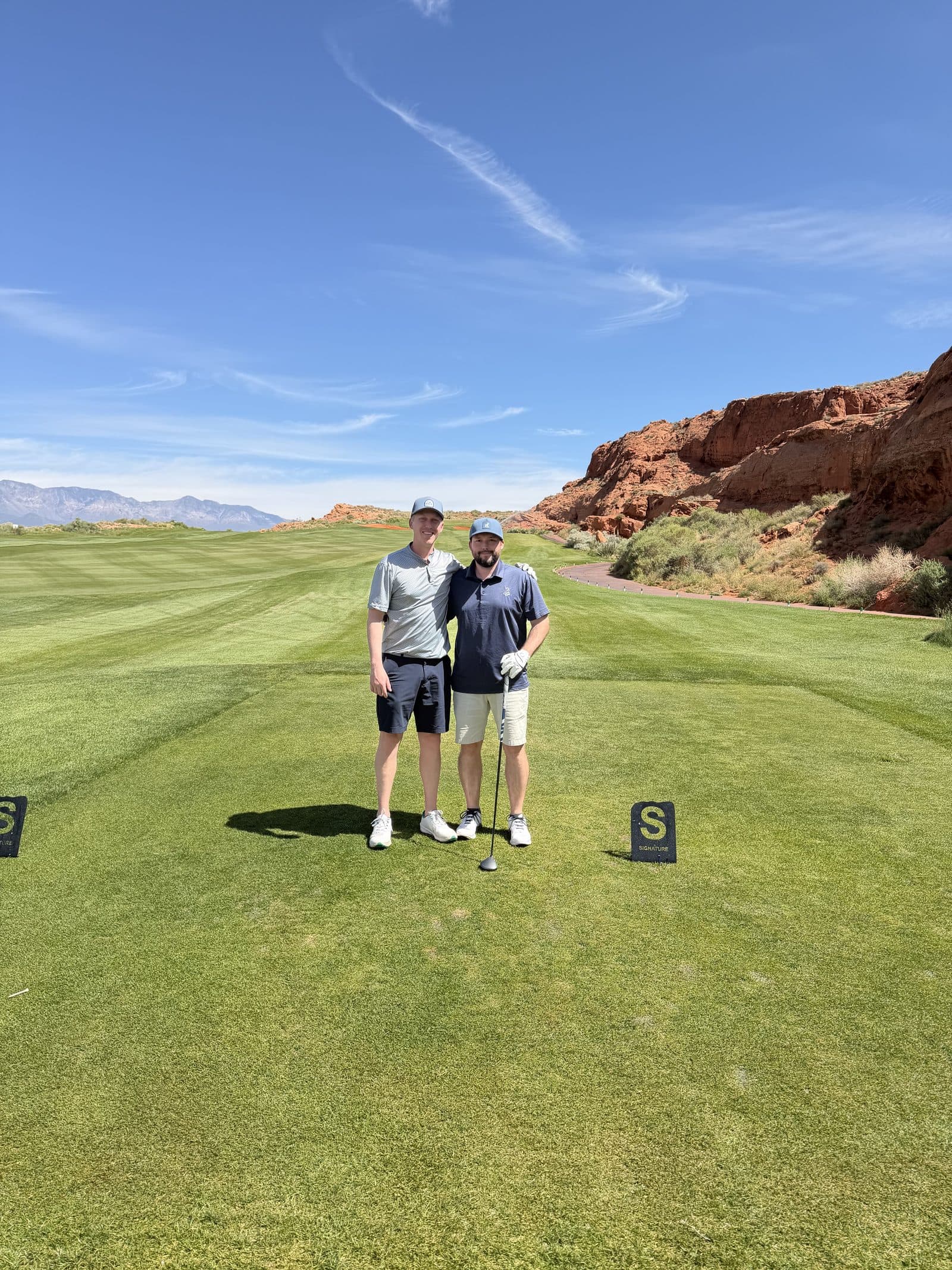 Two golfers standing on a tee box at a red rock desert golf course.