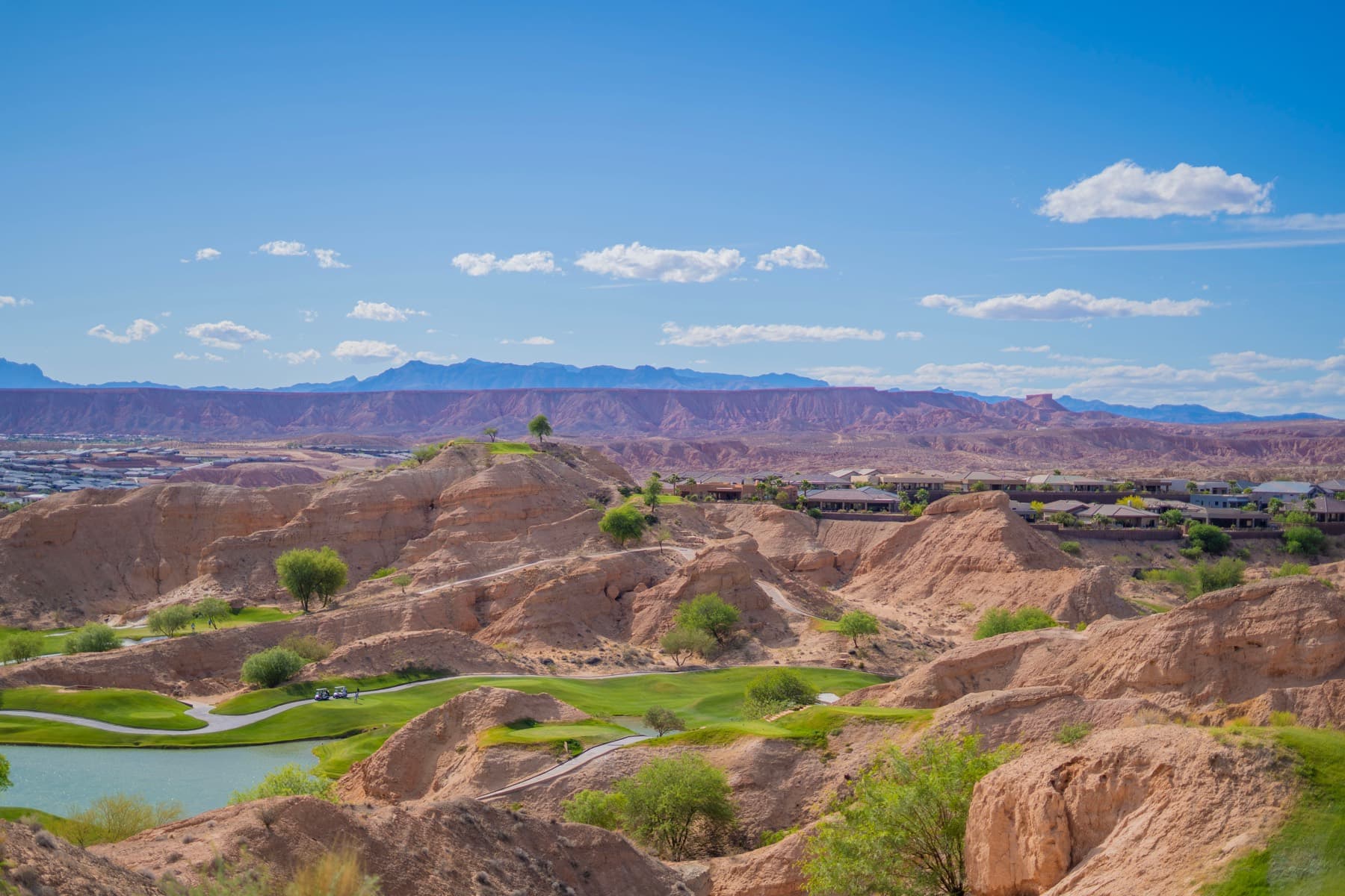 A wide desert golf fairway with white bunkers and red rock hills.